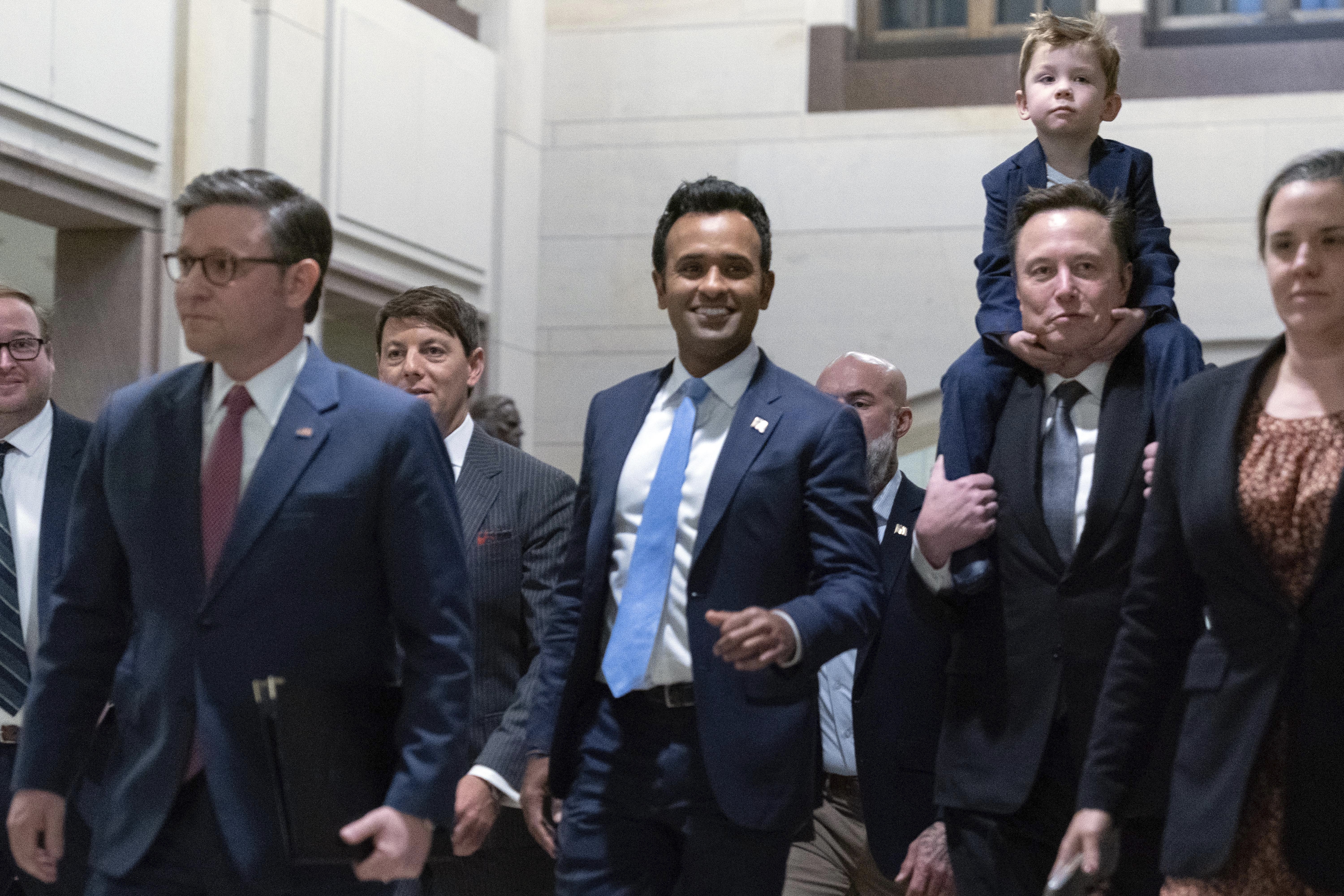 Speaker Mike Johnson (left), walks with Vivek Ramaswamy (center) and Elon Musk, who is carrying his son on his shoulders as they arrive for a roundtable meeting to discuss President-elect Donald Trump's planned Department of Government Efficiency.